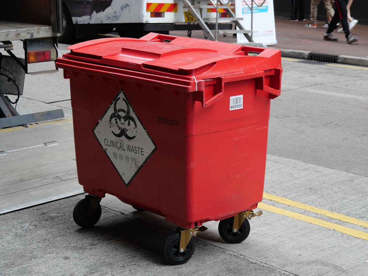 A red clinical waste bin labeled with biohazard symbol on a city street indicating proper waste management.